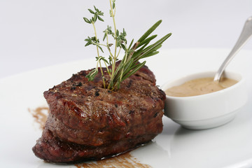  Delicious steak medium rare with rosemary leaves and sauce on a white background.