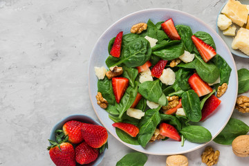 salad with strawberry, spinach leaves, parmesan cheese and walnuts on concrete background. healthy...