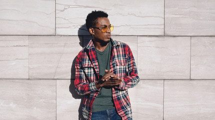 Portrait stylish african man wearing red plaid shirt, looking away, guy posing on city street, gray brick wall background