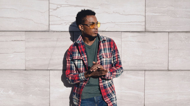 Portrait stylish african man wearing red plaid shirt, looking away, guy posing on city street, gray brick wall background