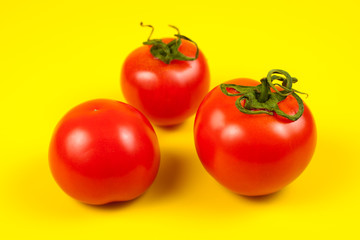 Fresh red tomato with green stem on yellow background