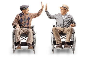 Two senior men in wheelchairs giving high-five