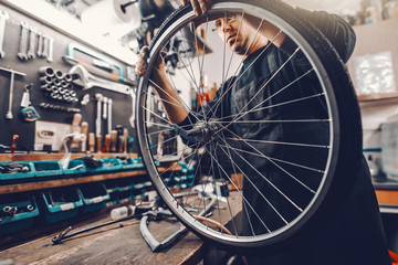 Caucasian dedicated man putting tyre on bicycle wheel while standing in workshop.