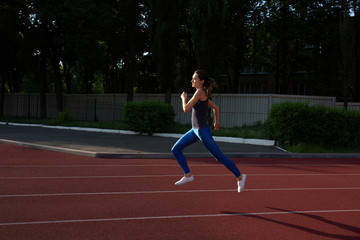 Obraz premium Athletic girl wearing sport apparel running at the empty stadium at the evening. Space for text