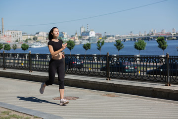 Sporty brunette woman running on the bridge near the river. Space for text