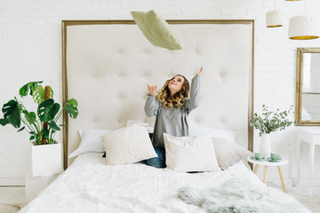 Naklejka premium Beautiful young caucasian European woman having fun throwing pillow in the air at home