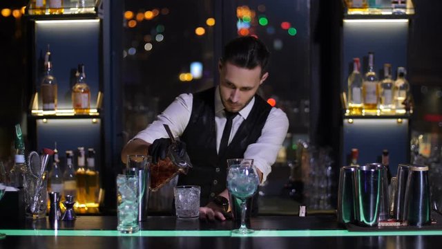 Professional bartender prepared Negroni cocktail and pouring it to oldfashioned glass at bar of modern nightclub. Barman working at bar counter