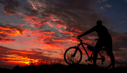 Obraz premium cyclist with a bicycle, in the background fiery sunset.