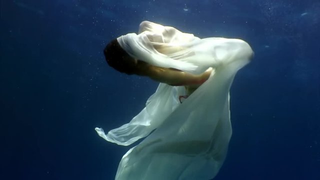 Young woman underwater model in white cloth on background of blue water. Concept of creativity and art of creating images.