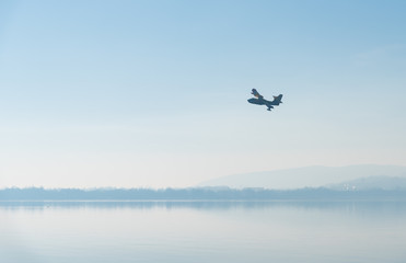Fototapeta na wymiar Silhouette of a plane flying against a blue sky over the lake in fog.
