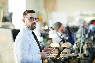 Waist up portrait of bearded factory worker wearing lab coat  standing in industrial workshop, copy...