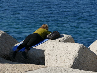 Turista stanca mentre riposa sotto il sole sugli scogli in riva al mare in una bella giornata di primavera