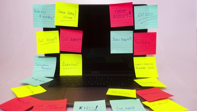 Busy office day with post-it notes or a to do list of tasks and reminders that needs to done as illustrated by colorful sticky notes stuck on the laptop computer