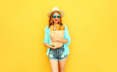 portrait happy smiling young woman holding paper bag with long white bread baguette, wearing straw hat, shorts on colorful yellow background