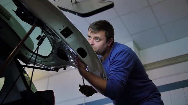 Paintless Dent Repair. A male master is repairing a dent on the hood of a car without painting with a quality crochet tool with a red handle in an auto repair shop isolated. New technology, machine