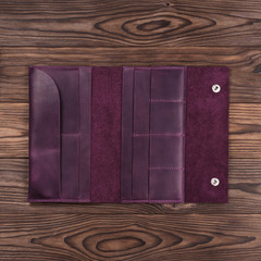 Purple handmade travel wallet lies on textured wooden backgroud closeup. Wallet is open and empty. Up to down view. Stock photo of businessman accessories.