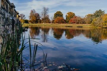 Beautiful autumn garden with tree reflections in water, old stone wall. Hever Castle Gardens, Kent,...