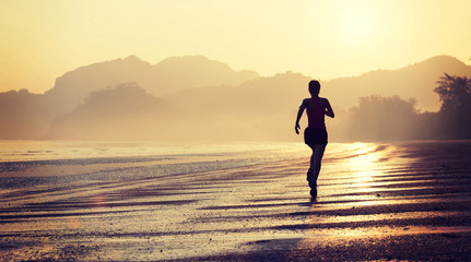 Silhouette of young fitness woman running at sunrise beach