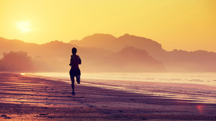 Silhouette of young fitness woman running at sunrise beach