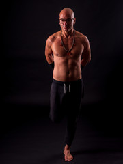 Fototapeta na wymiar Buddhist monk practicing yoga on black background in long pants and glasses