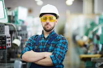 Waist up portrait of bearded factory worker wearing hardhat posing in workshop standing with arms crossed, copy space