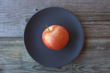  Fresh red apple on a dark color plate over the old wooden table. Fruit harvest. Minimalism.