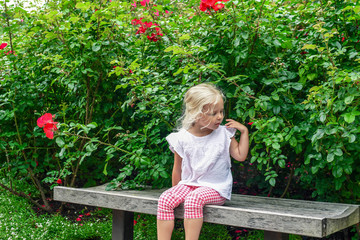 Little blonde girl sitting on a bench in the garden