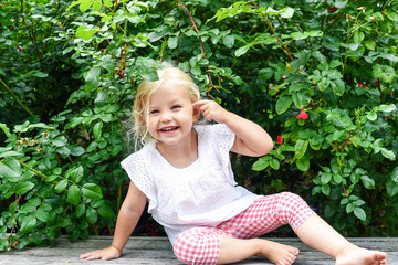 Naklejka premium Happy little girl sitting on a bench in the garden