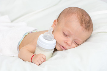 newborn baby curled up sleeping on a blanket with feeding bottle
