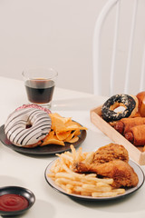 fast food and unhealthy eating concept - close up of hamburger or cheeseburger, deep-fried squid rings, french fries, drink and ketchup on wooden table