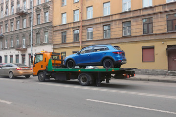 Fototapeta na wymiar tow truck carrying a blue car on a city street