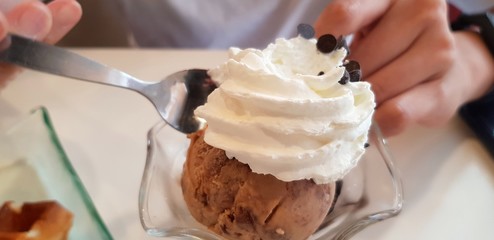 Close up people using spoon to eat chocolate ice cream with whipped cream on top - Refreshment and Cold or dessert food 