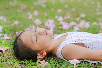 Pretty little girl sleeping on green grass with fall pink flower in the garden outdoor.