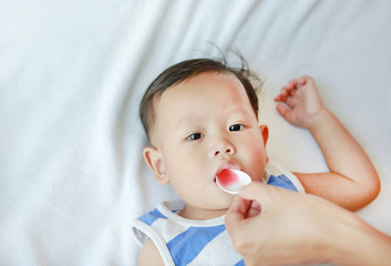 Asian baby boy takes medicine syrup from a spoon. Sick child.