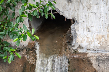 Water flows from a large hole in the wall of water canal.