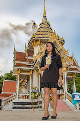 Young woman in black dress standing in front of crematorium in Buddhist monastery with smoke rising...