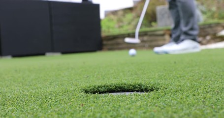 Golf Putting - putting stroke with first attempt missing the whole, second attempt into the hole.  Close up of hand retrieving the golf ball.
