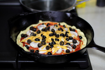 Pizza with pepperoni, mushrooms, and black olives ready to bake in the oven.