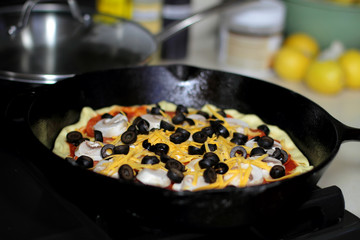 Pizza with pepperoni, mushrooms, and black olives ready to bake in the oven.