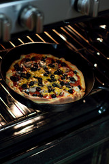 Freshly baked homemade pizza with pepperoni, mushrooms, and black olives in cast iron pan from the oven.