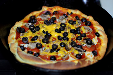 Freshly baked homemade pizza with pepperoni, mushrooms, and black olives in cast iron pan from the oven.