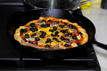 Freshly baked homemade pizza with pepperoni, mushrooms, and black olives in cast iron pan from the oven.