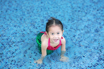 Fototapeta na wymiar Happy little Asian child girl in a mermaid suit lying poolside with looking camera.