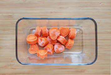 Frozen baby food homemade, Orange heart from carrot Cubes in square glass bowl on wooden board.