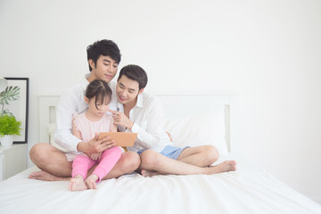 Asian Male gay couple using tablet with their daughter in bedroom