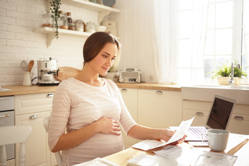 Optimistic positive young single pregnant female at last months of pregnancy doing finances, paying...