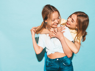 Two young beautiful smiling blond hipster girls in trendy summer colorful T-shirt clothes. Sexy carefree women posing near blue wall in. Positive models having fun and hugging