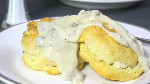 Spooning country gravy with sausage bits onto hot biscuits