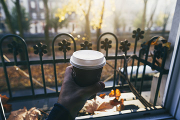 Male hand holding cup of coffee morning sun against the window