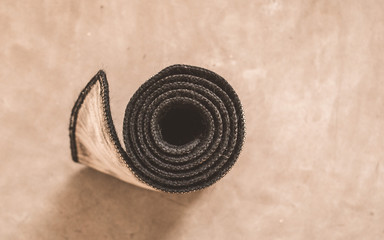 Fototapeta na wymiar Rolled yoga mat after exercise isolated on rustic cement floor background in a sport activity center. Fitness, Healthy life, keep fit, lifestyle wellness concept. Top view. Copy space room for text.